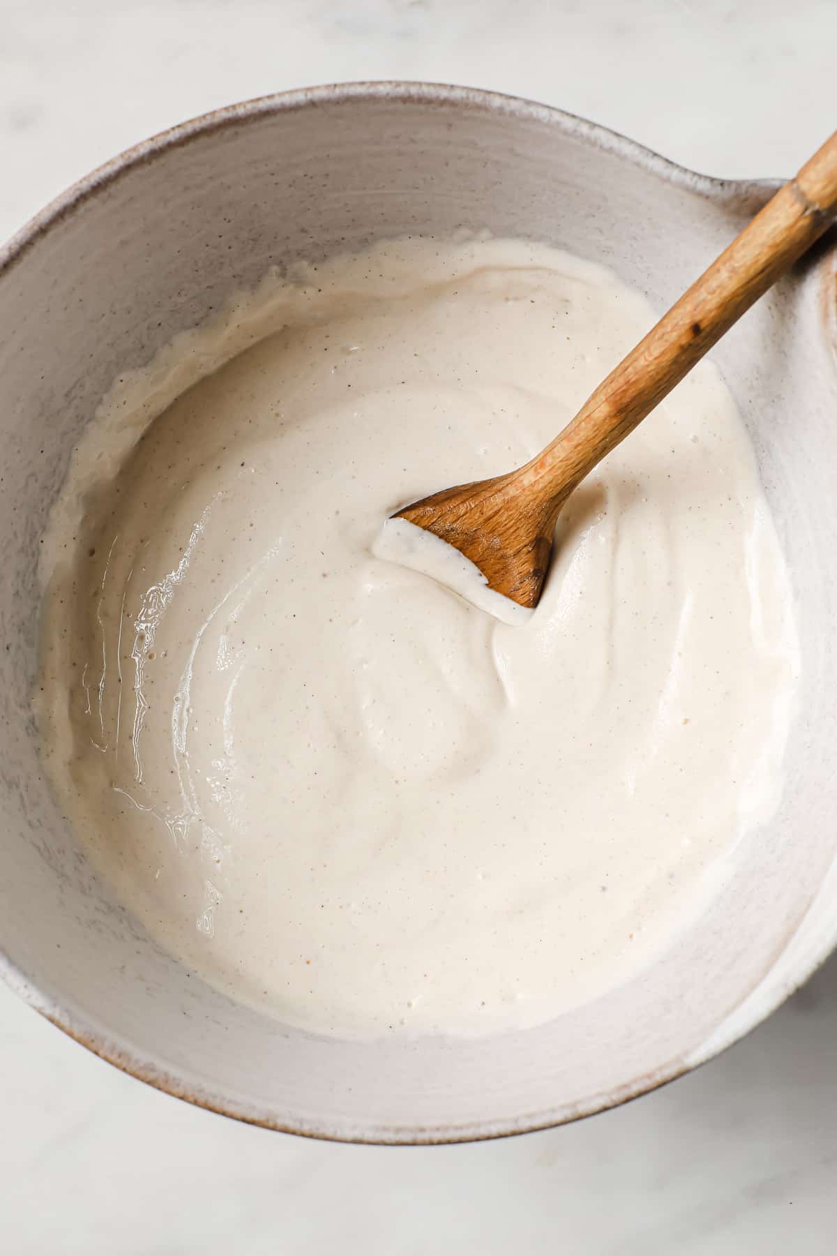 A mixing bowl full of cheesecake batter, with a wooden spoon.