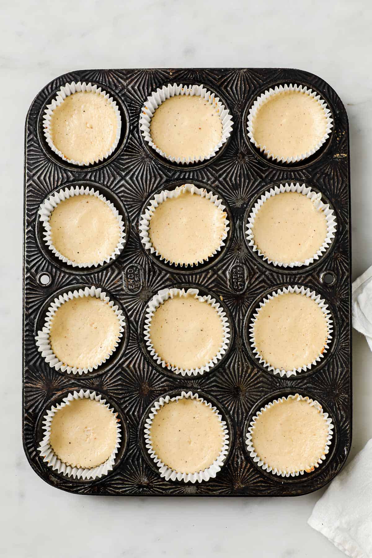 A muffin tin lined with muffin liners, filled with freshly baked mini cheesecakes.