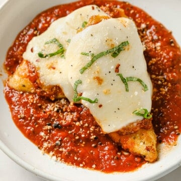 A white bowl with a plate of breaded chicken with melted cheese in a pool of marinara sauce.
