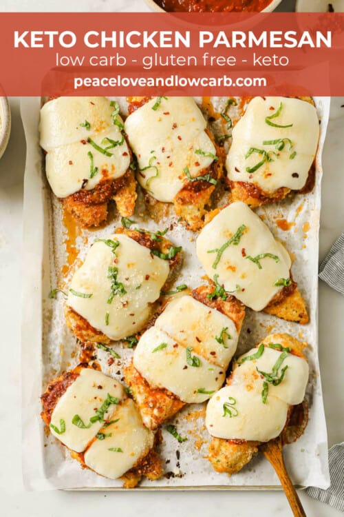 A sheet pan lined with parchment paper, topped with breaded chicken breasts, topped with marinara and cheese.