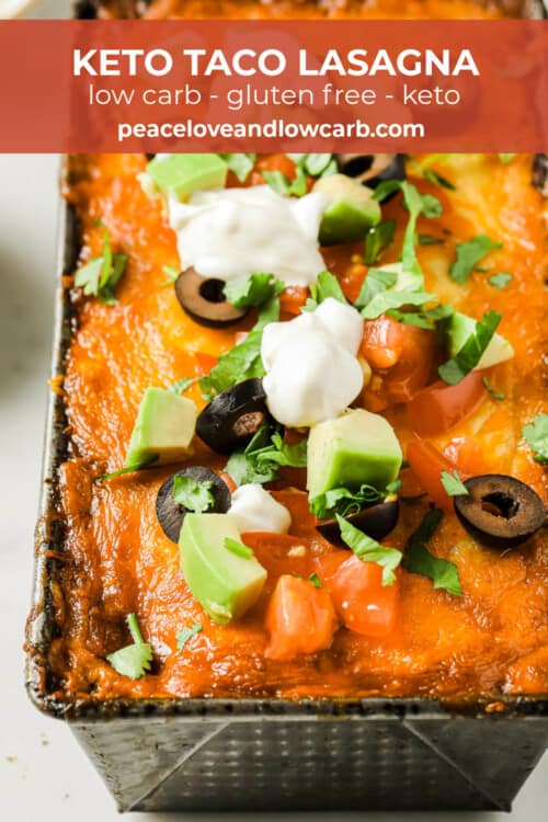 A loaf pan full of low carb lasagna, topped with golden brown baked cheese, olives, avocado, tomato, and sour cream.